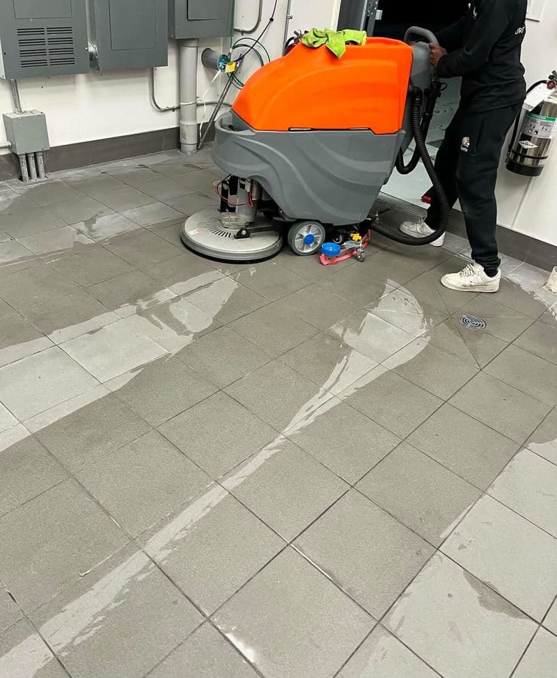 Ride-on floor scrubber machine cleaning a tiled commercial floor