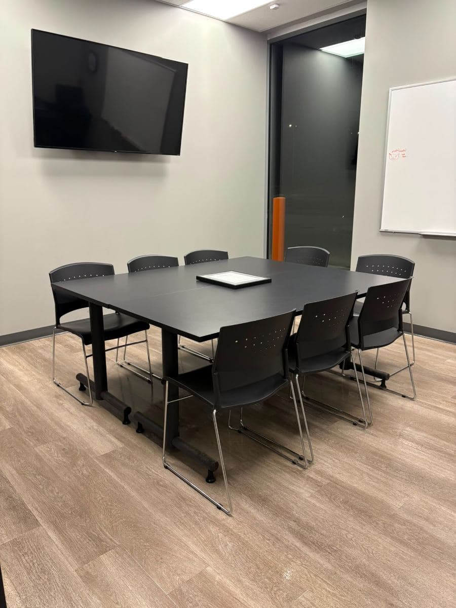 Office meeting room after an evening clean, with a dark boardroom table, stacking chairs and a wood-effect floor
